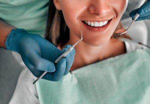 Tannlegens hender holder instrumenter nær pasientens munn.