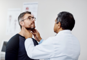 Mannlig lege undersøker utvendig en mannlig pasient sin hals.